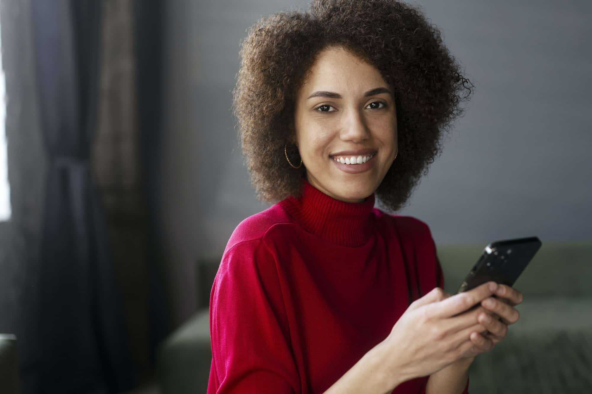 African American woman in red casual attire, using mobile phone, working online, text messaging