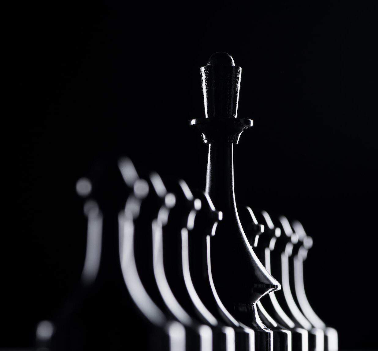 silhouettes of chess pawns and queen isolated on black, business concept
